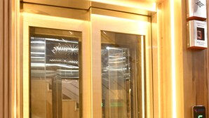An elevator with a digital display, wooden paneling, and a fire alarm switch. - Brij Inn (Varanasi)