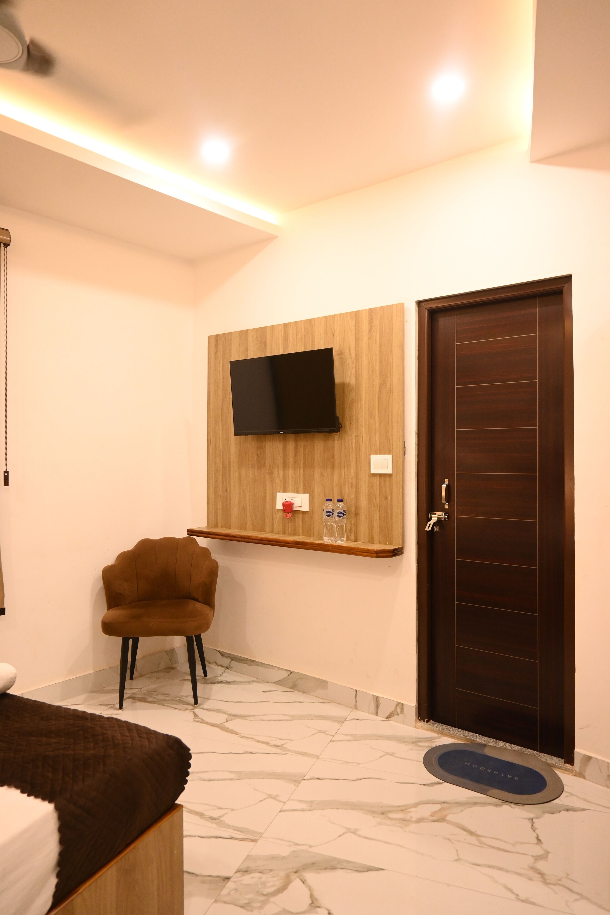 Une salle de bain moderne avec un meuble-lavabo en bois, un téléviseur fixé au mur, une chaise marron et une porte en bois foncé.