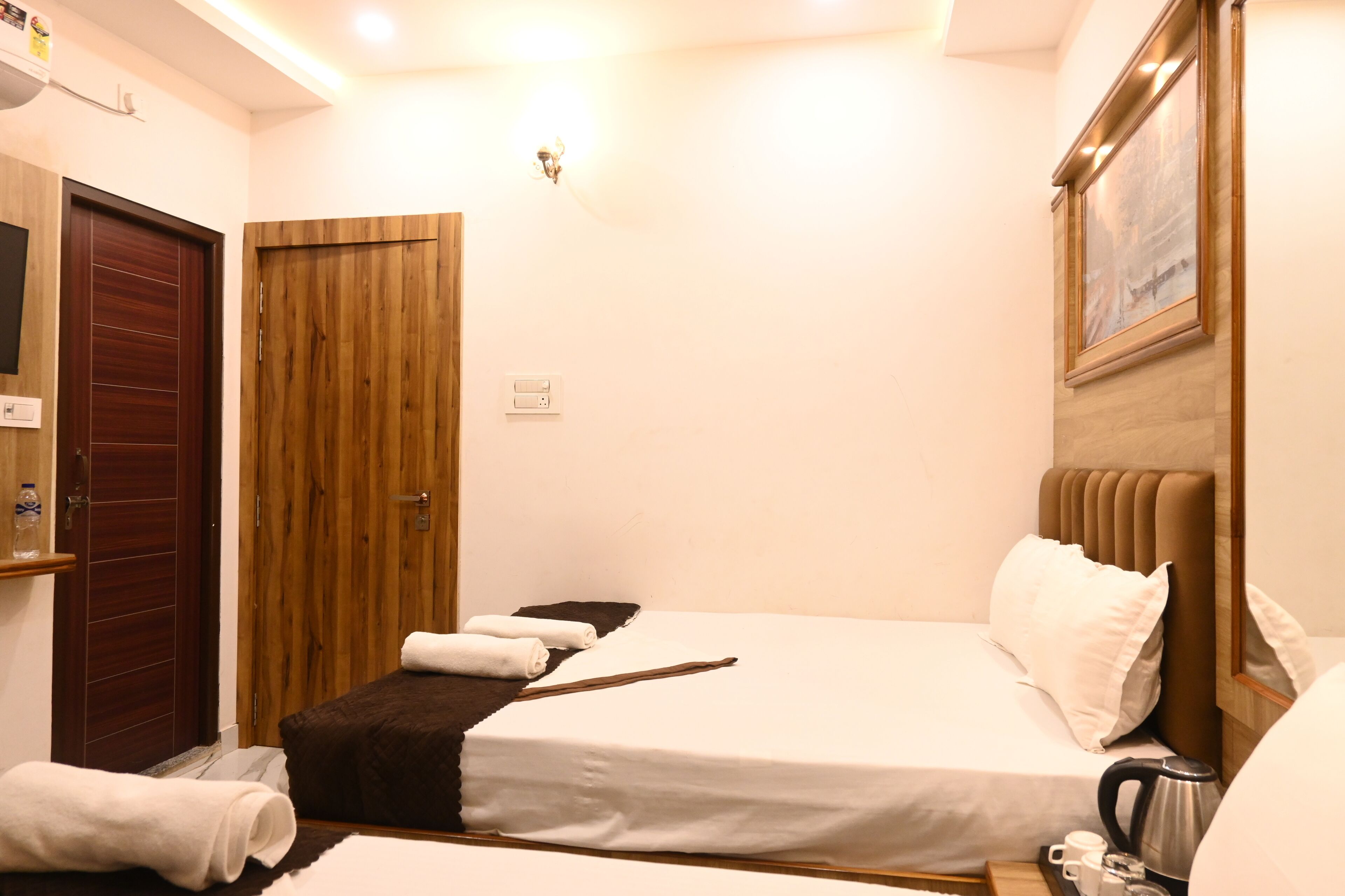 Une chambre d’hôtel avec deux lits, une porte en bois, un luminaire fixé au mur et un tableau.