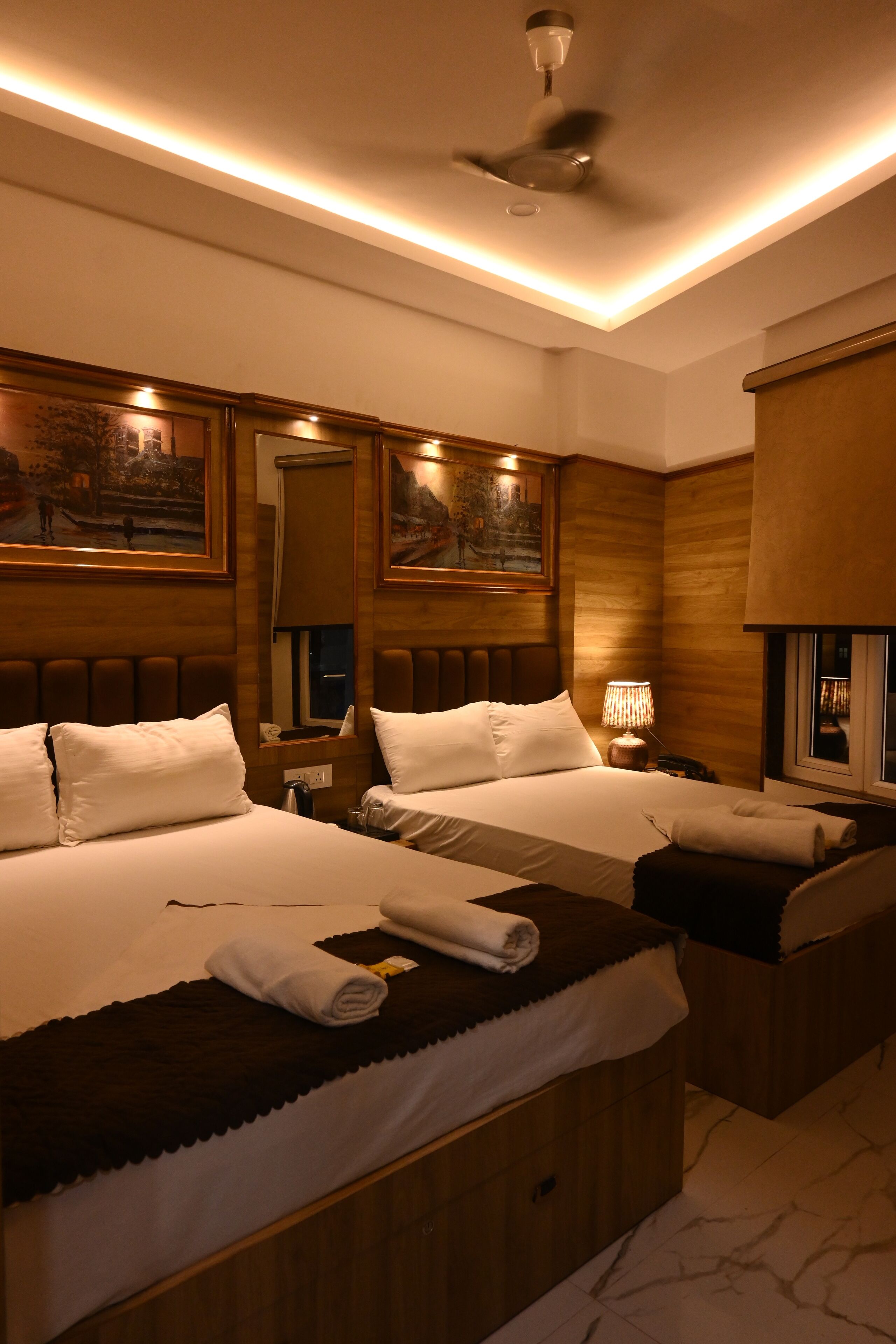A hotel room with two beds, a ceiling fan, and artwork on the walls.