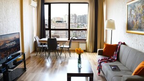 Quarto de hotel moderno com uma janela grande, área de refeições, sofá e TV.