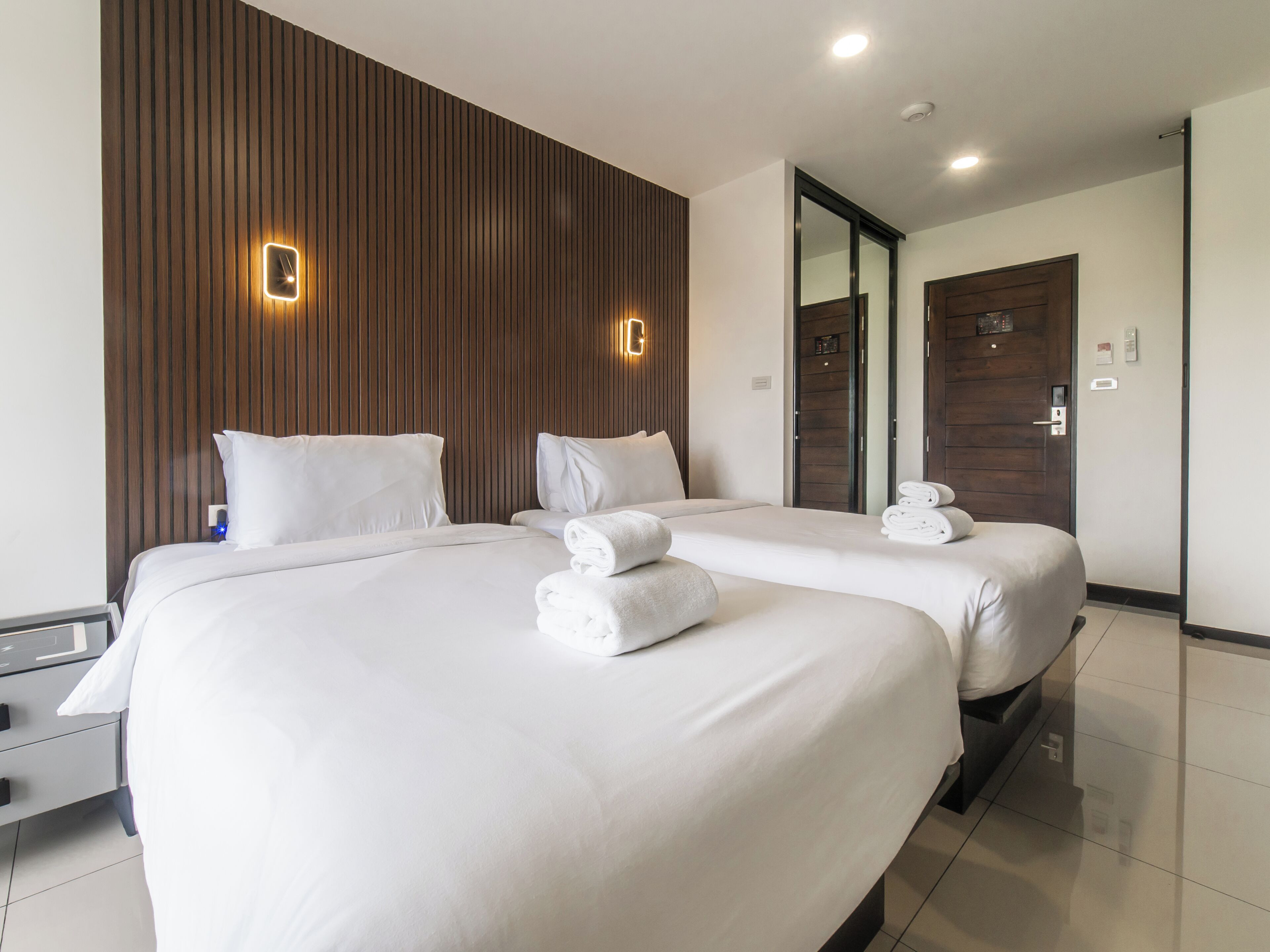 A hotel room with two beds, a wooden accent wall, a mirror, and a door with a handle.