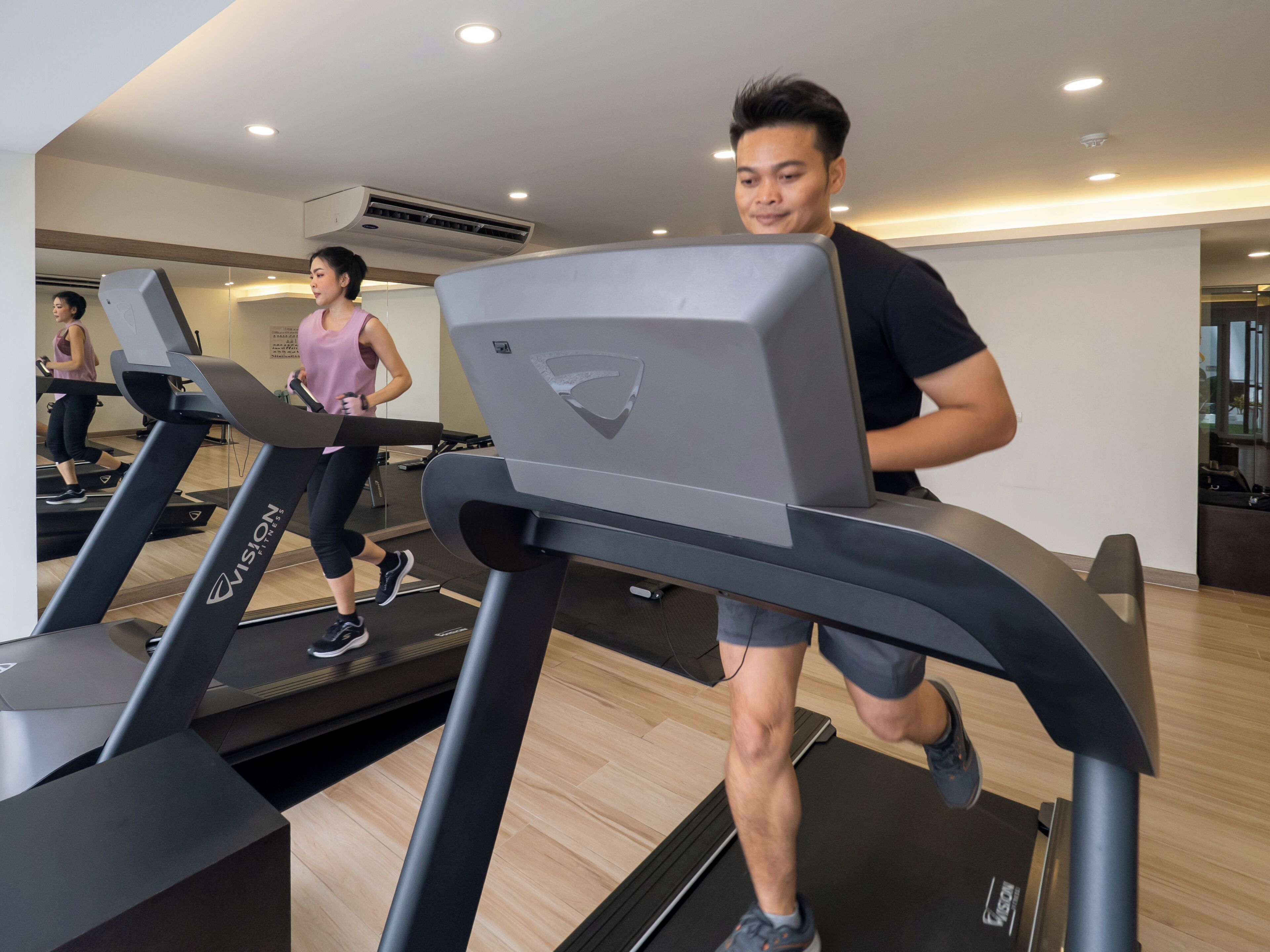 A gym with treadmills, a woman exercising, and a man running on a treadmill.
