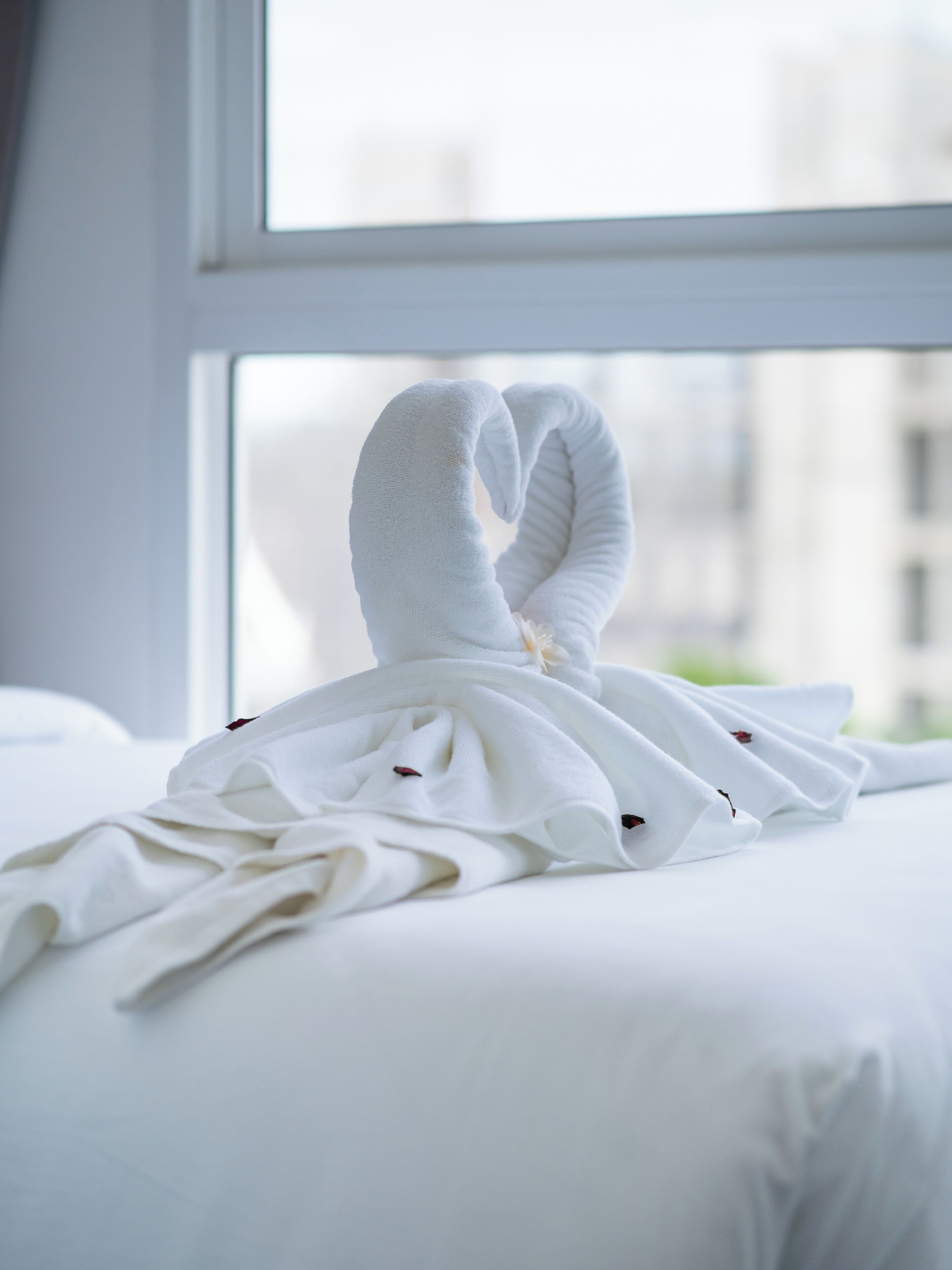 A neatly made bed with a towel arranged in a heart shape.