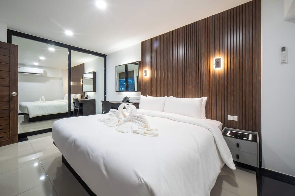 A modern hotel room with a large bed, a desk, and a mirror.