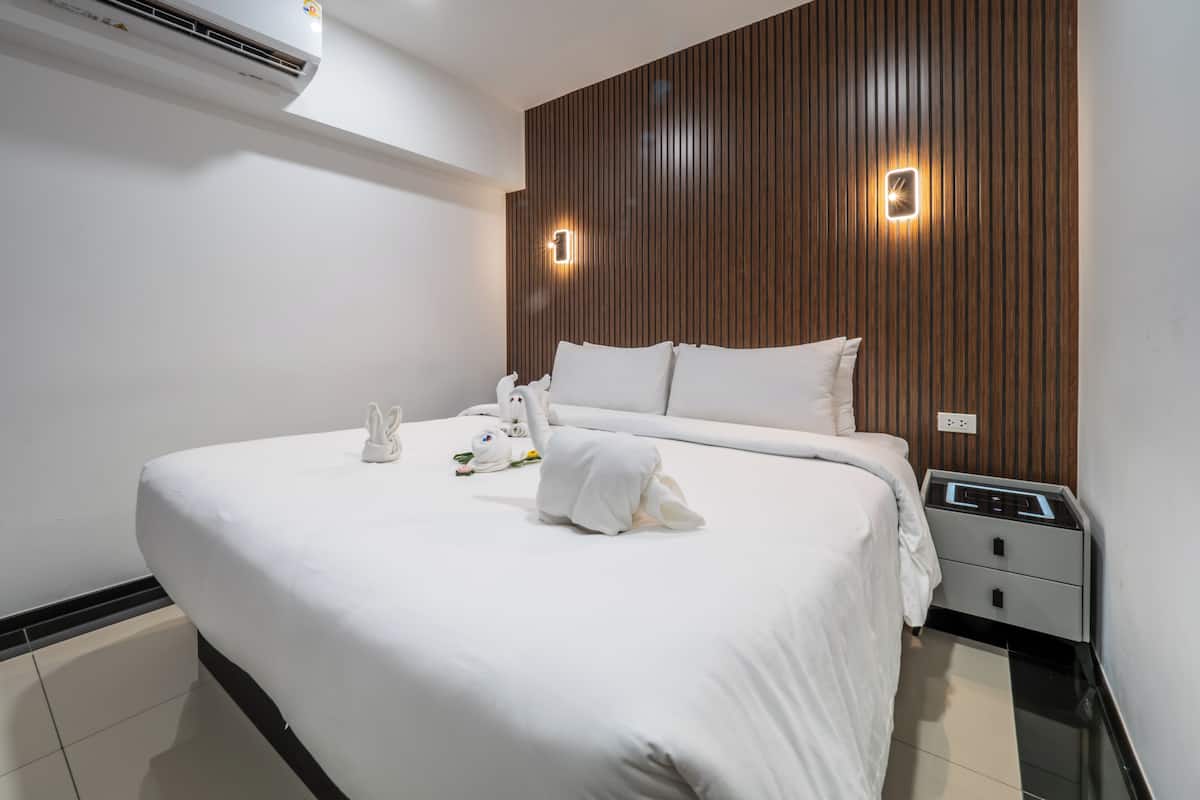 A modern hotel room with a large bed, wooden panel wall, and a nightstand with a lamp.