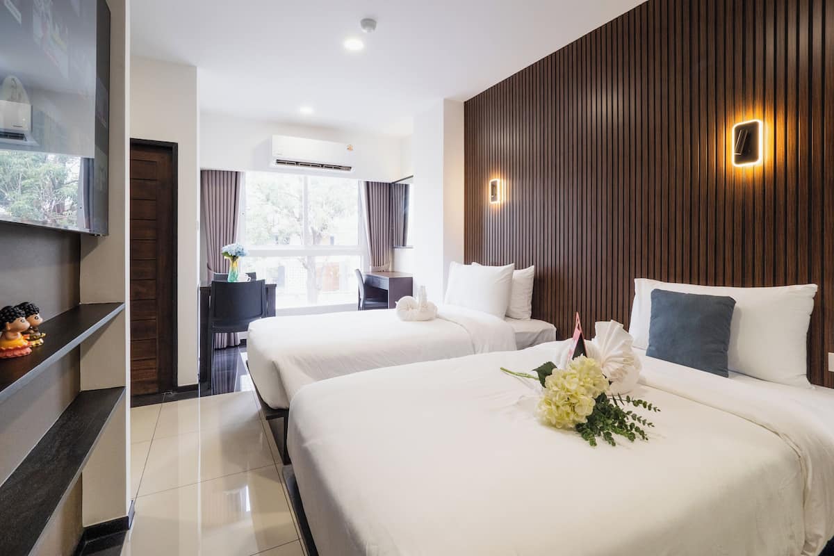 A hotel room with two beds, a TV, a desk, and a window with curtains.