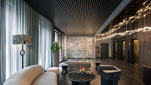 Eine moderne Lobby mit einer gebogenen Couch, einem runden Couchtisch mit Blumen und einer dekorativen Lichtinstallation an der Decke.