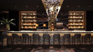 Eine Bar mit einer zentralen Theke, zahlreichen Flaschenregalen und Barhocker.