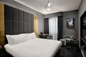 Een moderne hotelkamer met een groot bed, een klein bureau, een stoel, een televisie en een raam met gordijnen.