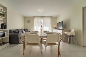 Un espace repas avec une table dressée pour quatre personnes, un canapé, un téléviseur et un coin cuisine.