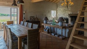 Un coin repas rustique avec une table en bois et des chaises en osier, un mur en pierre et une cheminée.