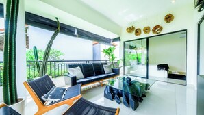 A modern living room with a sofa, two chairs, a glass coffee table, and a balcony with a view of greenery. - STEP OUT OF THE ORDINARY SoHo meets- Berawa -Canggu BALI (Bali)