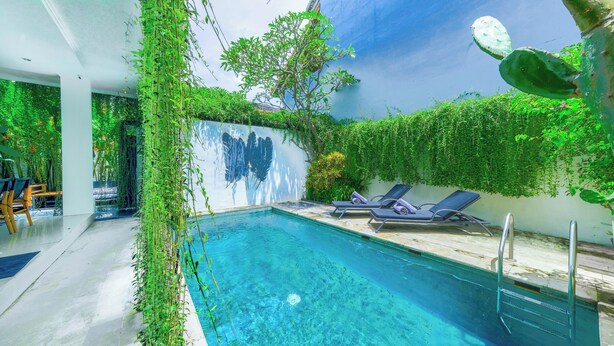 A swimming pool with clear water, surrounded by lush greenery and a white wall with a mural. - STEP OUT OF THE ORDINARY SoHo meets- Berawa -Canggu BALI (Bali)