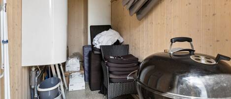 A compact kitchen with a large grill, a white refrigerator, and a wicker chair.