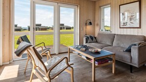 A living room with a sofa, two chairs, a coffee table, and a large window offering a view of buildings and a grassy area.