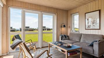 Un salon comprenant un canapé, deux fauteuils, une table basse et une grande fenêtre donnant sur des immeubles et un espace verdoyant.