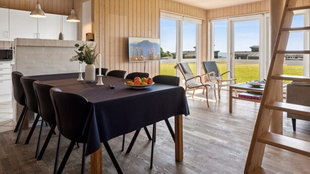 A modern dining area with a wooden table, black chairs, and a view of the outdoors through large windows.