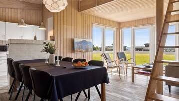 Un espace de salle à manger moderne, avec une table en bois, des chaises noires et une vue sur l’extérieur grâce à de grandes fenêtres.