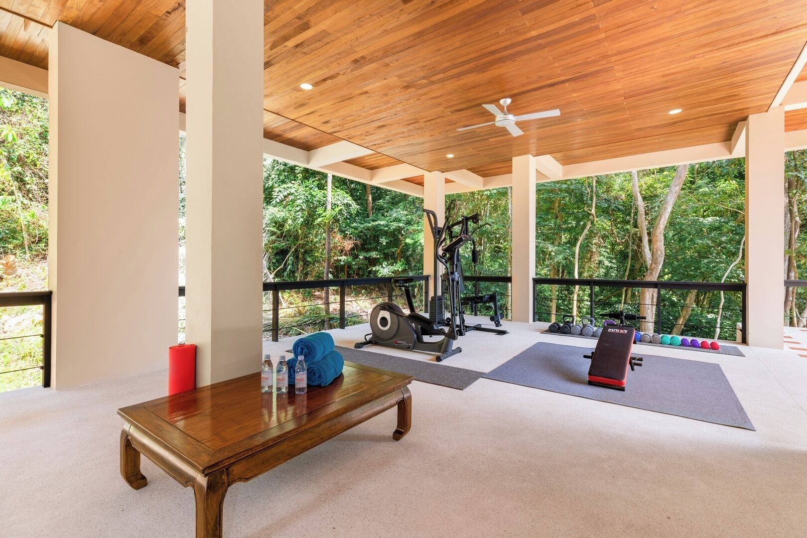 A gym with exercise equipment, a wooden table, and a view of trees.