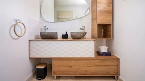 Un baño moderno con tocador de madera, dos lavamanos de piedra, un espejo grande y un mueble de madera.