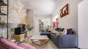 Una sala de estar moderna con sofá, sillón y mesa de centro. Se observa una estantería y un mapa mundial en la pared.