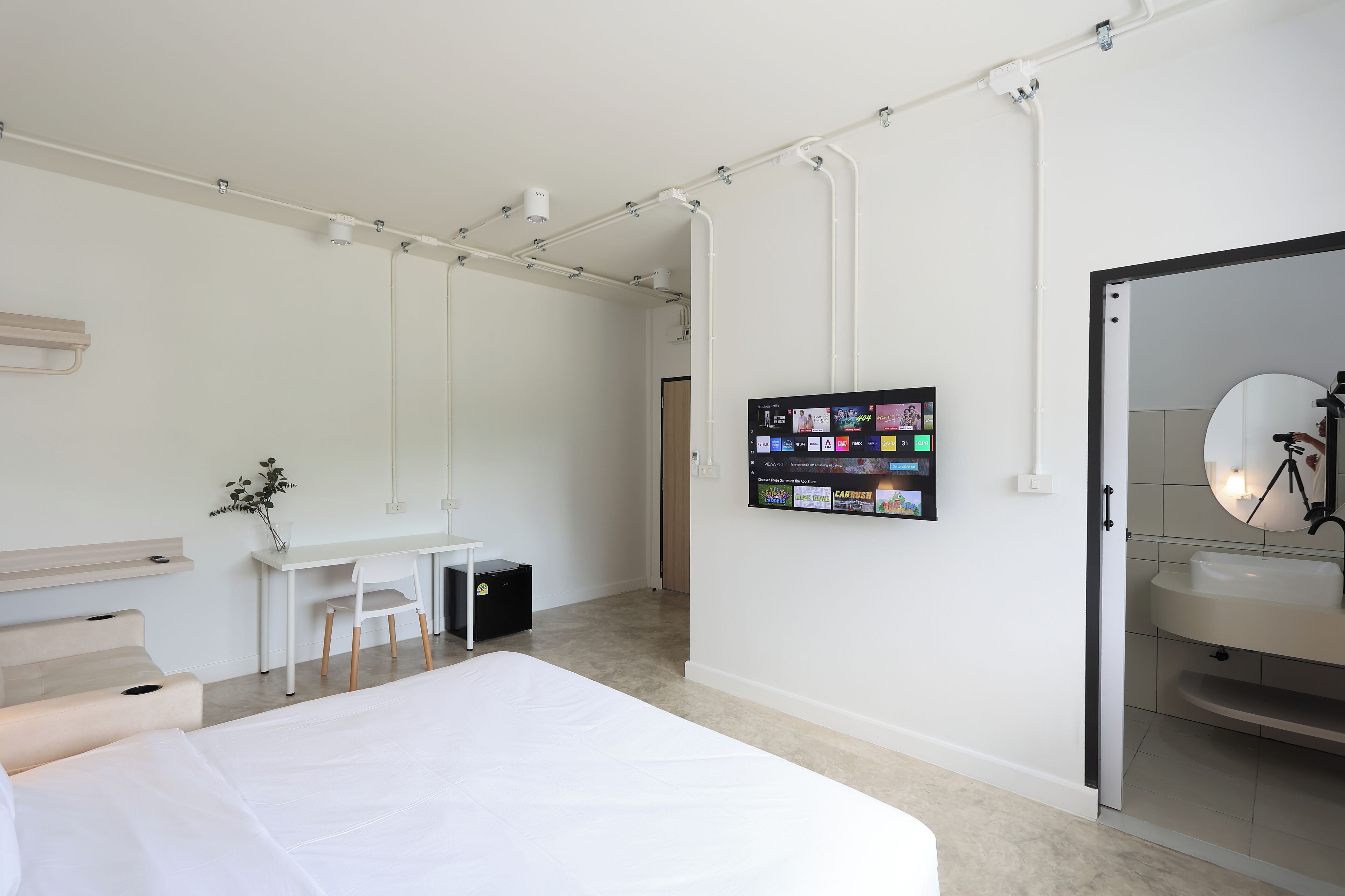 Een moderne hotelkamer met een bed, bureau, stoel, een klein tafeltje, een aan de muur bevestigde televisie en een badkamer met een wastafel en spiegel.