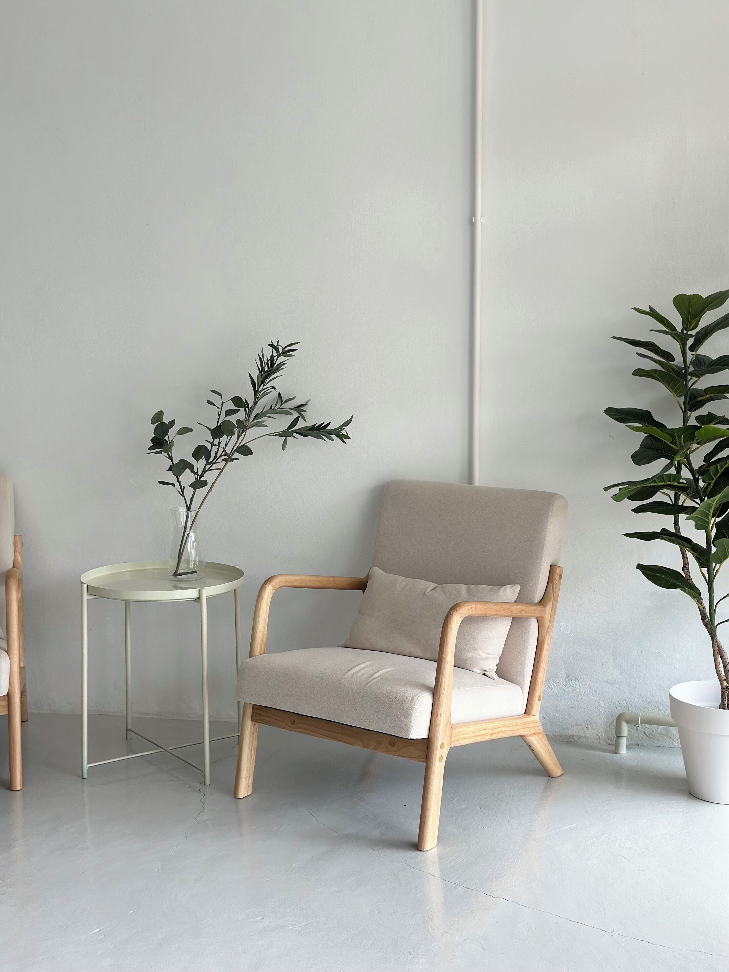 Un salon moderne avec un fauteuil de couleur claire, une petite table ronde ornée d’un vase de plantes vertes et une plante en pot.