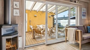 Een gezellige kamer met een houtkachel, een schuifdeur naar een terras buiten met rieten meubels en een houten terras.