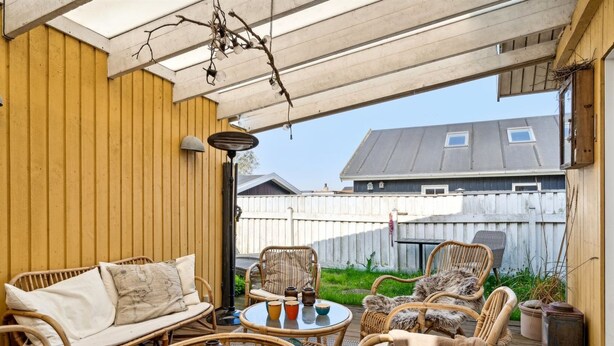 Un espace extérieur aménagé, abrité et doté de meubles en osier et d’une table en verre, offrant une vue sur une cour arrière avec une clôture en bois et une maison.