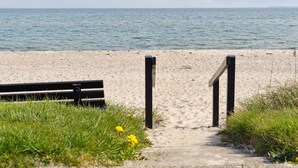 Een zandstrand met een houten bankje en een pad dat naar het water leidt.