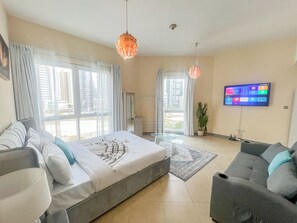 A modern hotel room with a large bed, a sofa, a TV, and a balcony with curtains. - Snug Studio With City Views, Perfect For Couples (Dubai)