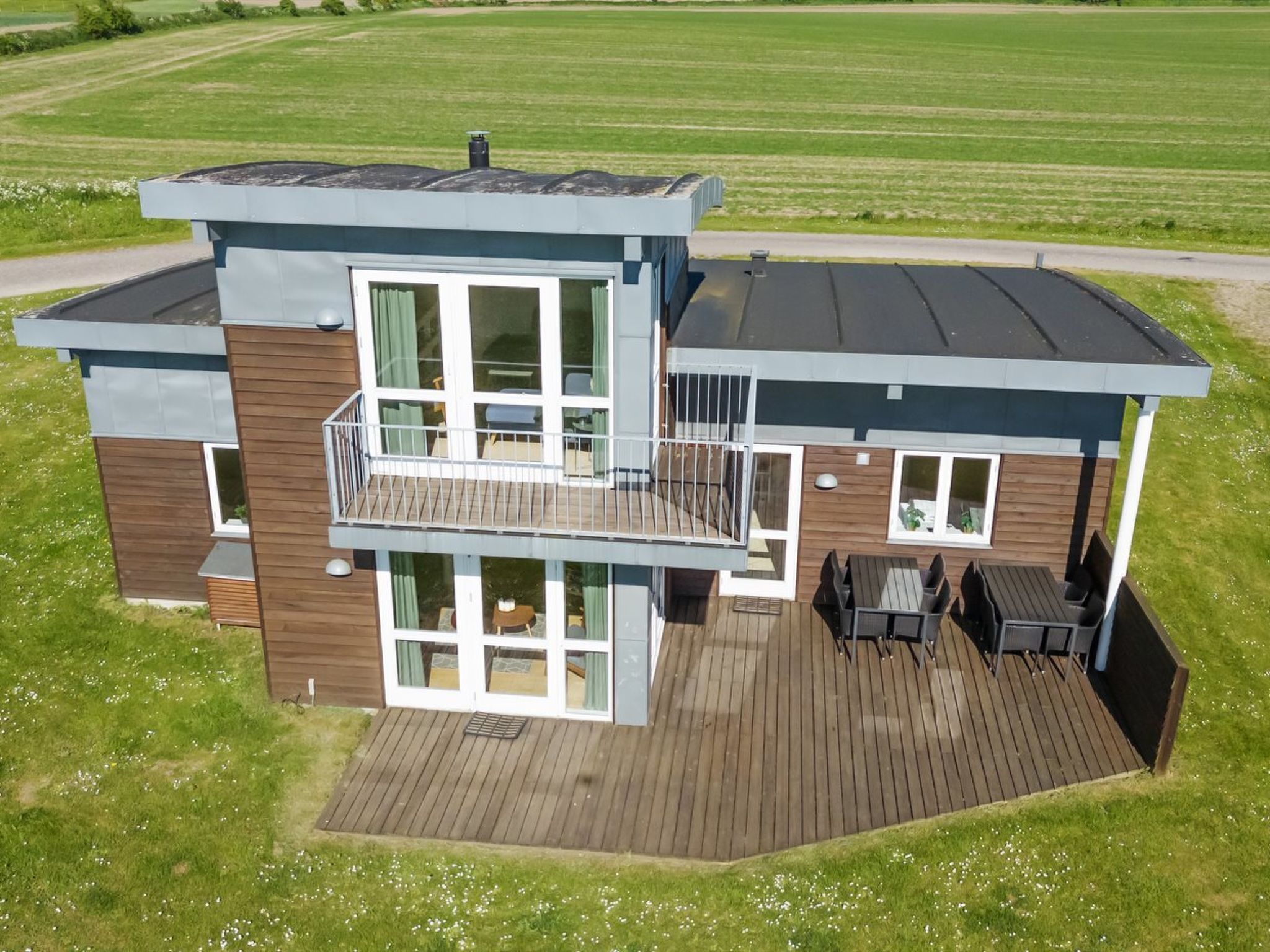 Een modern huis met twee verdiepingen, een balkon, grote ramen en een houten terras.