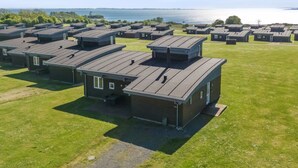 A row of modern, single-story cabins with flat roofs, arranged in a linear fashion on a grassy field with a body of water in the background.