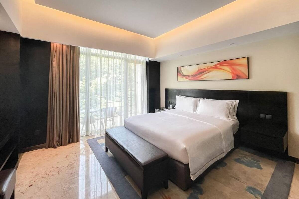 Ein modernes Hotelzimmer mit einem großen Bett, einer Sitzbank, einem Nachttisch und einem Fenster mit Vorhängen.