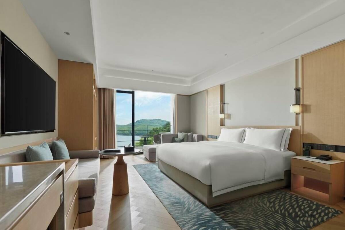 Ein modernes Hotelzimmer mit einem großen Bett, einem Schreibtisch, einem Stuhl und Blick ins Freie.