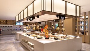 Um restaurante moderno com um balcão central exibindo diversos pratos, iluminação suspensa e um interior limpo e organizado.
