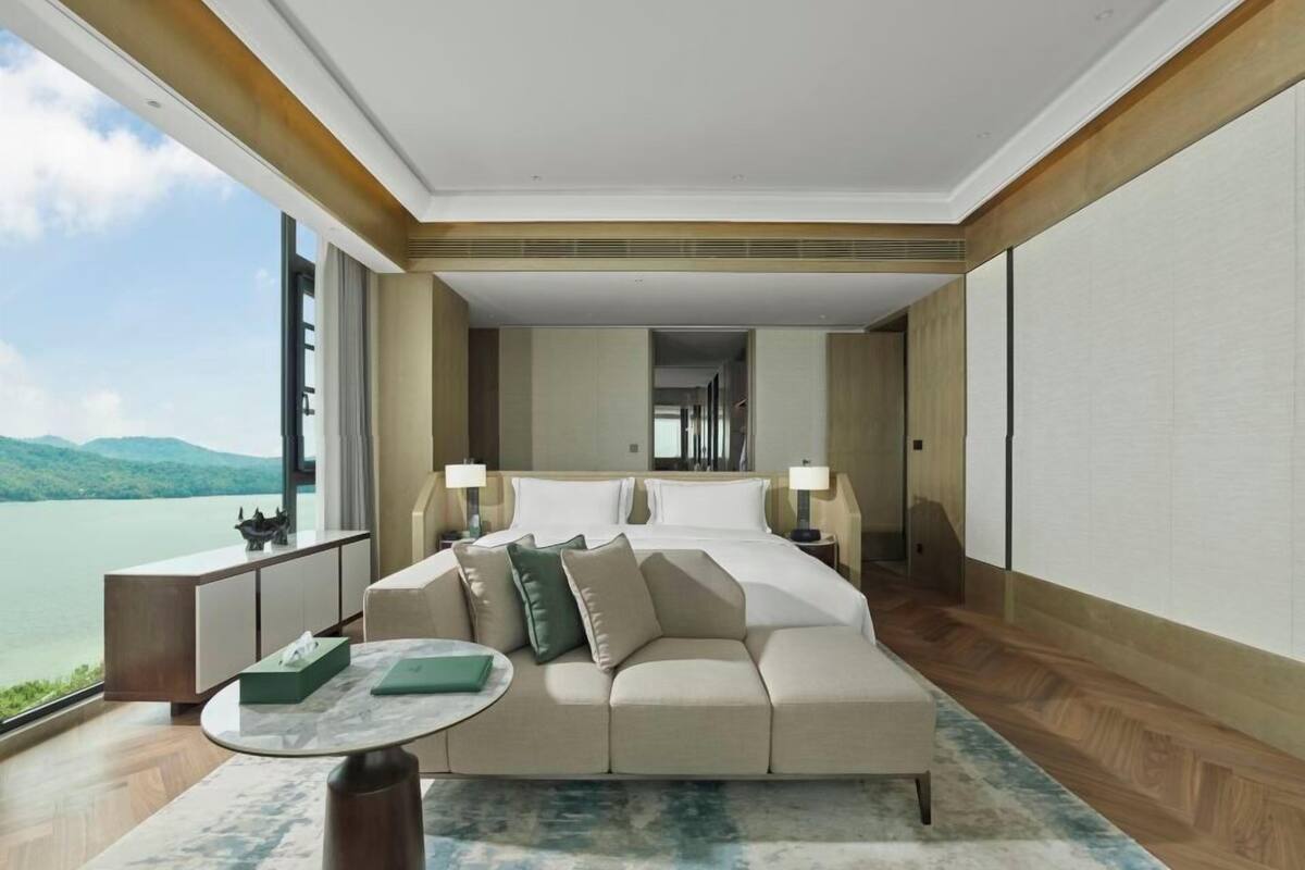 Ein modernes Hotelzimmer mit einem großen Bett, einer Couch, einem kleinen Tisch und Blick auf einen See.