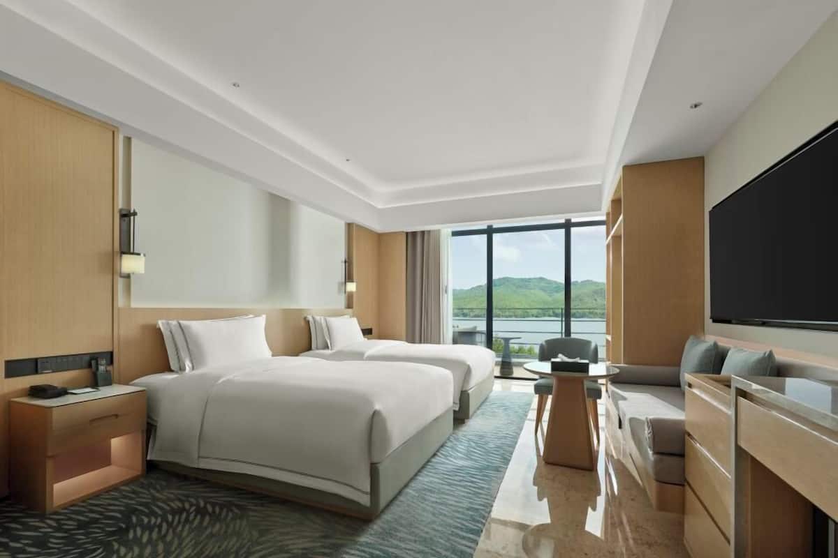 Ein Hotelzimmer mit zwei Betten, einem Fernseher, einem Schreibtisch und Seeblick.