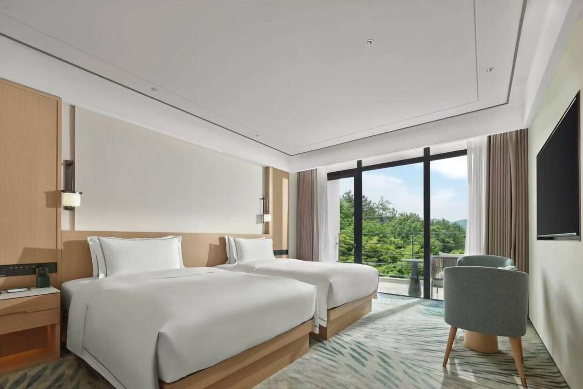 Ein modernes Hotelzimmer mit zwei Betten, einem großen Fenster mit Ausblick, einem Flachbildfernseher und einem kleinen Tisch.