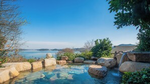 Piscina ao ar livre cristalina com pedras e cascata, rodeada por vegetação e vista para a água.