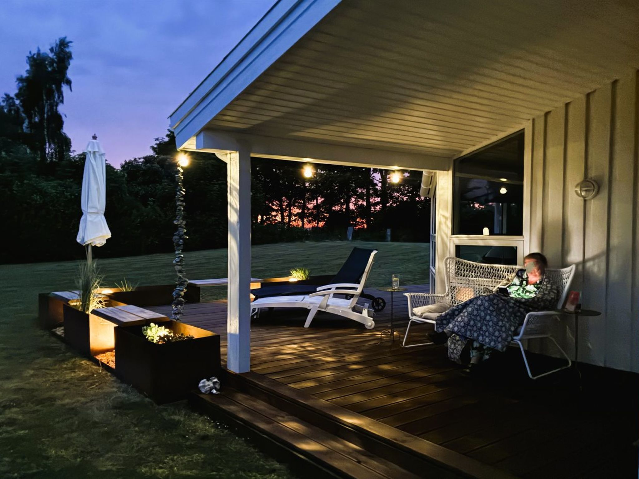 A covered outdoor area with a wooden deck, two lounge chairs, and a person seated.
