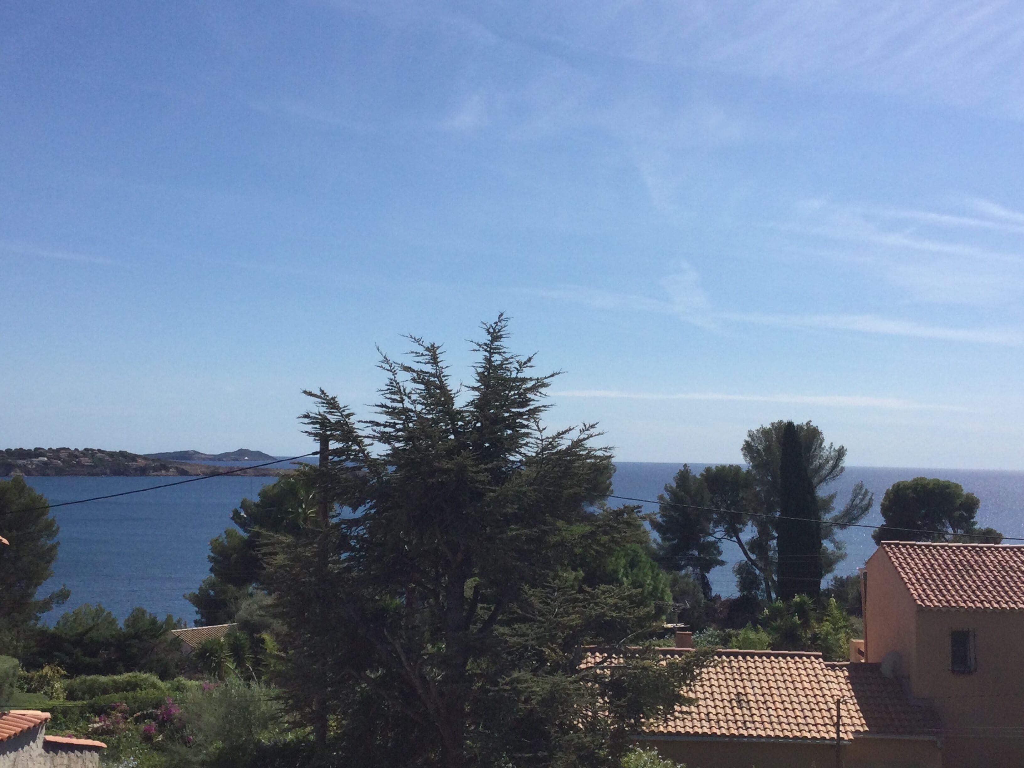 A coastal view with a clear sky, a body of water, and a building with a tiled roof.