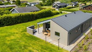 Ein modernes Haus mit einer großen Terrasse und einem überdachten Außenbereich, umgeben von üppiger Vegetation und Blick aufs Meer.