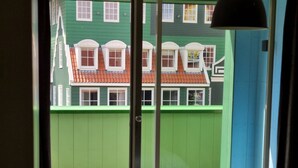 Een kamer met een bed en uitzicht op een gebouw met groene begroeiing en rode daken, en een schuifdeur.
