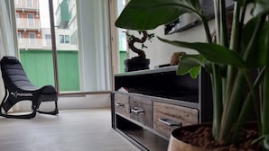 Een moderne woonkamer met een zwarte Playseat stoel, een houten kast en een grote potplant.