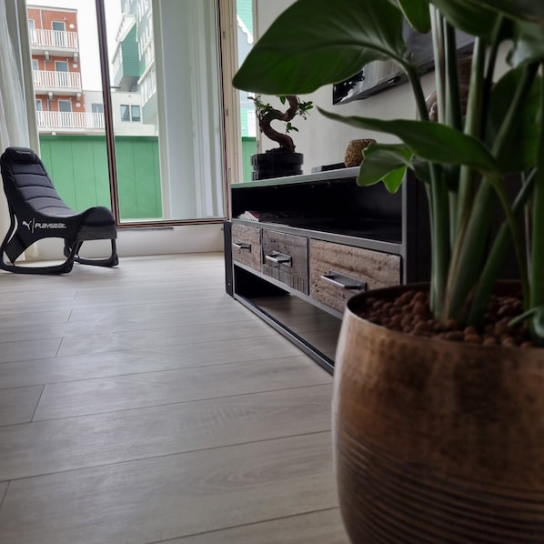 A modern living room with a black Playseat chair, a wooden cabinet, and a large potted plant.