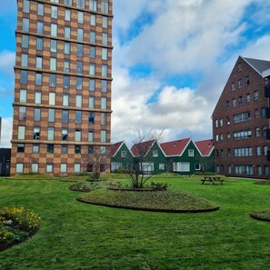 A modern building complex with a mix of brick and glass facades, a central green lawn with a circular garden, and a clear sky. - Hermitage Suits & Apartments - Amsterdam Zaandam (Zaandam)