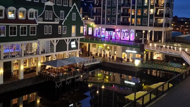 Een gebouw aan het water met meerdere verdiepingen, balkons en een restaurantgedeelte met terras.