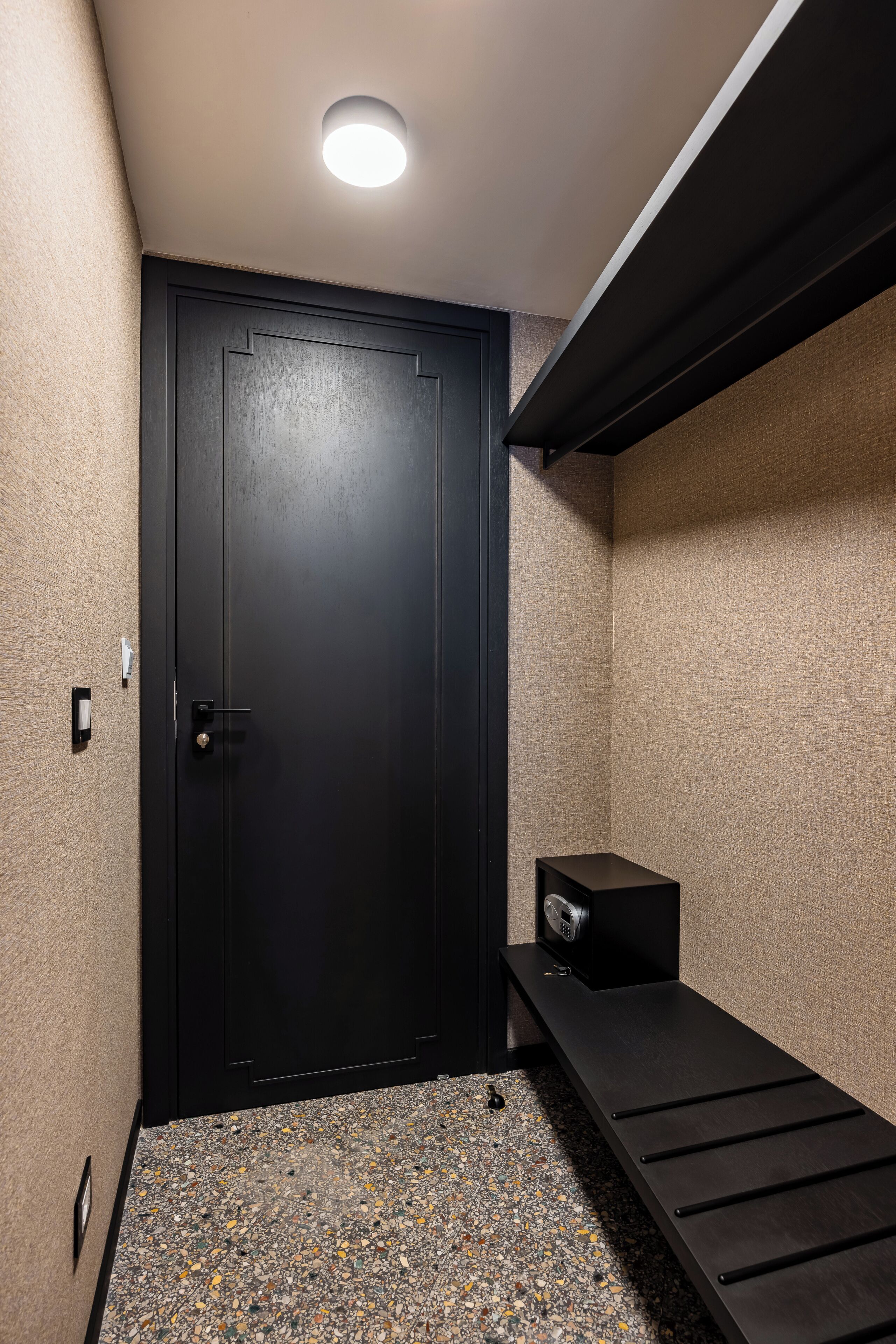 A compact room with a black door, a small bench, and a ceiling light.